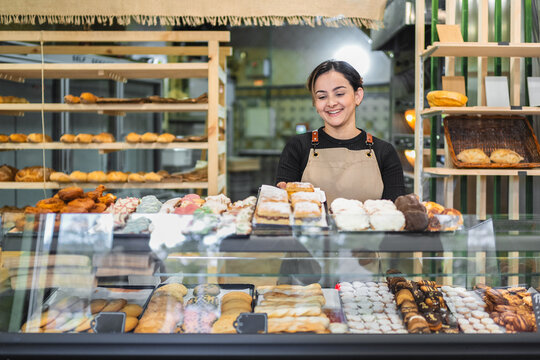 Smiling baker arranging pastries in display case at bakery shop