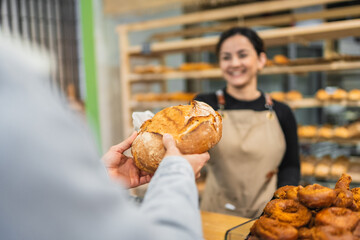 Baker giving freshly baked bread to customer in bakery shop