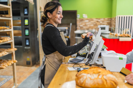 Baker working at cash register in bakery shop