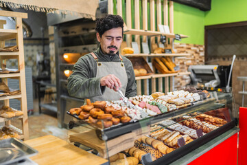 Baker arranging pastries in display case at bakery shop