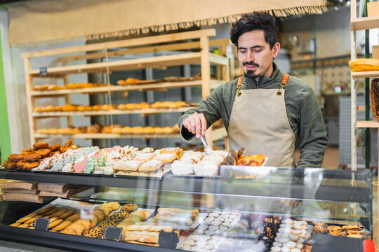 Baker arranging pastries in display case at bakery shop