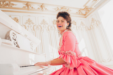Joyful woman in elegant pink gown playing piano in a luxurious room