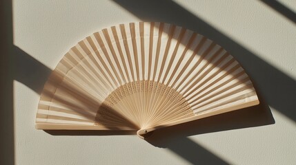 Photograph of a wooden fan lying on a beige wall. the fan is open, with the blades facing upwards and the handle resting on the surface.
