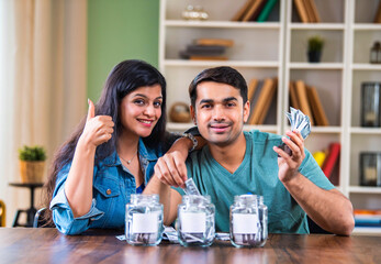 Indian couple placing cash in labeled jars, symbolizing smart budgeting and investment strategies