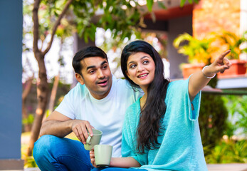 Happy Indian couple having coffee on a green porch, smiling and sharing quality time together