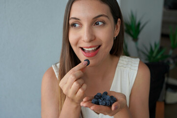 Close-up of young woman picking a blueberry from her hand. Looking to the side.