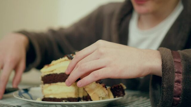 Man cutting layered cake with knife. Male slicing chocolate dessert on plate. Guy preparing to eat sweet pastry at table