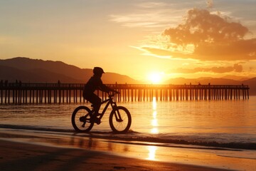 Fototapeta premium Bicyclist rides along the shoreline at sunset, with golden hues reflecting on the water near a distant pier