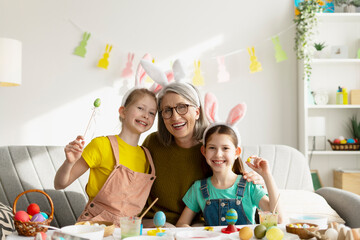 Happy grandmother and granddaughters painting easter eggs wearing bunny ears