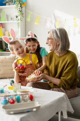 Grandmother and granddaughters painting easter eggs and eating candies
