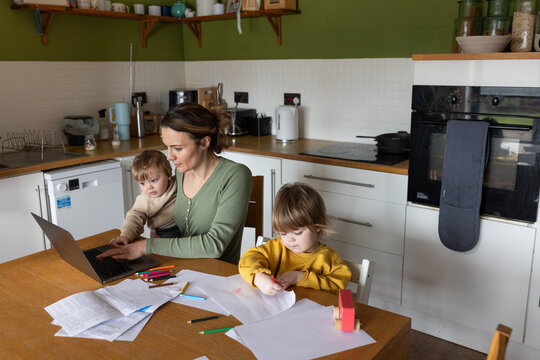 Mother working from home and multitasking caring for her young children