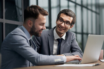 Fototapeta premium Two young businessmen sitting at workplace and working together in office