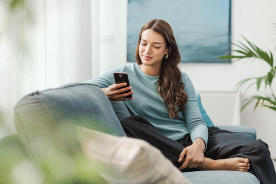 Beautiful young woman relaxing at home and using her smartphone