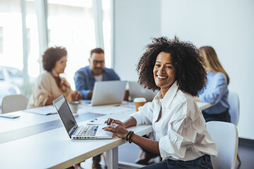 Smiling Professional Woman Working on Laptop in Office with Colleagues