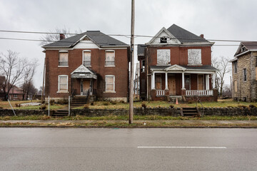 Two red brick vintage houses sitting abandoned on empty street with overcast sky in East St. Louis