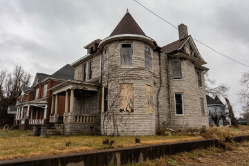 Vintage house with round turret front room boarded up on overcast day in East St. Louis