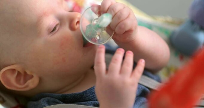 baby in blue holding and chewing on a teething toy, lies on a soft play mat, infant looks curious and engaged, exploring textures while soothing sore gums, home comfort, teething relief, baby care.