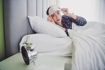 Young woman in pajamas waking up with a surprised expression while removing her sleep mask and...