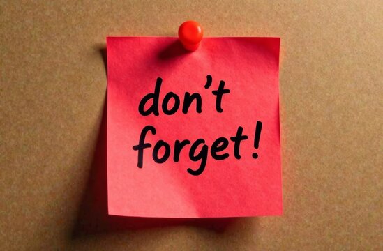A bright pink sticky note is pinned to a corkboard featuring the message don't forget! in bold black letters serving as a reminder for important tasks or events.