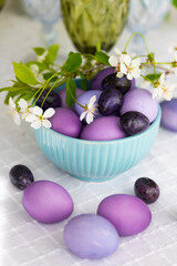 Easter eggs in shades of lilac and purple with green blooming branch in festive or holiday table