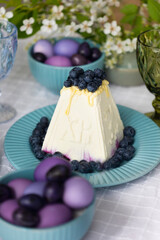 Holiday laid table for Easter with Russian traditional dish called Easter made of cottage cheese, painted eggs in shades of lilac and purple with green blooming branch