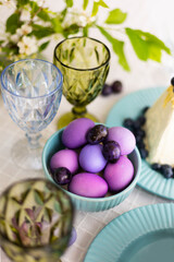 Easter eggs in shades of lilac and purple with green blooming branch in festive or holiday table