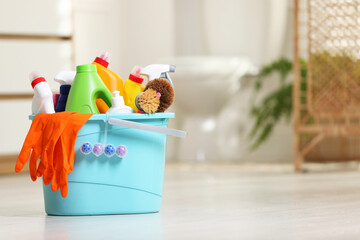 Bucket with different cleaning supplies on floor in bathroom, space for text