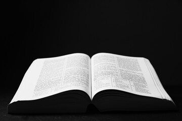Fototapeta premium Open Holy Bible in English language on black table, closeup