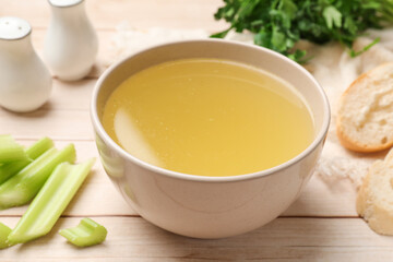 Tasty chicken bouillon in bowl, bread and ingredients on wooden table, closeup