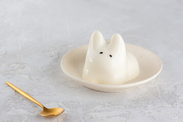 Jiggly cat dessert in a plate with golden spoon on a gray table. Dancing jelly animal mousse panna cotta. Popular Korean, Japanese pudding.