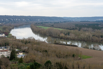 Obraz premium Beautiful view of the Seine River winding through La Roche-Guyon while trees stand bare in early spring under a cloudy sky