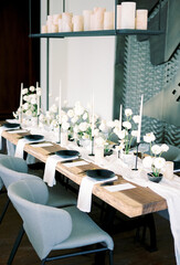 Set festive table in a restaurant with white flowers on a narrow tablecloth with candles on a hanging stand