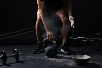 Man with talcum powder on hands training with kettlebell against black background, closeup