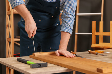Relaxing hobby. Man working with wooden plank and screwdriver at table indoors, closeup