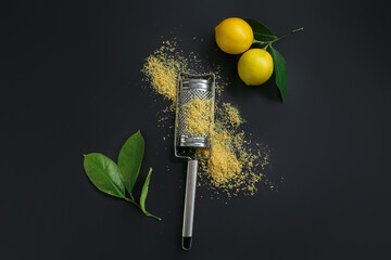 Grater with lemon zest, fresh fruits and leaves on black background, flat lay