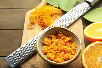 Orange zest, grater and fresh fruit pieces on wooden table, closeup