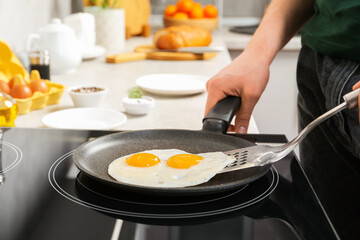 Man taking fried eggs from frying pan in kitchen, closeup
