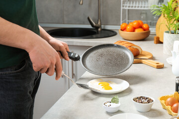 Man with frying pan putting tasty fried eggs onto plate in kitchen, closeup