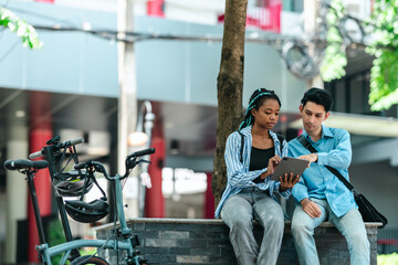 College students discuss work projects. Bicycle and electric scooter are parked nearby, suggesting an eco-friendly commute. Modern student lifestyle with technology and sustainable transportation
