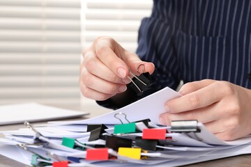 Woman attaching sheets of paper with metal binder clip at table, closeup
