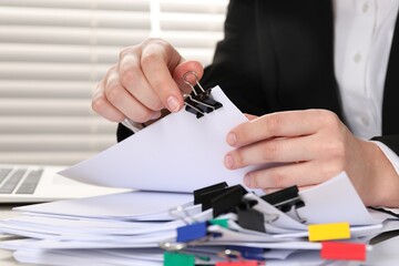 Woman attaching sheets of paper with metal binder clip at table, closeup