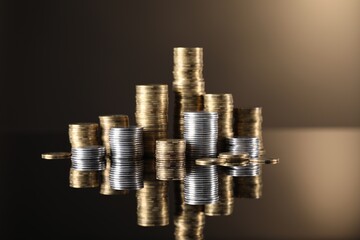 Stacks of different coins on light brown mirror surface, closeup