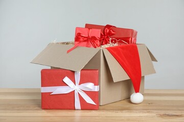 Parcel with gift boxes and Santa hat on wooden table against light background