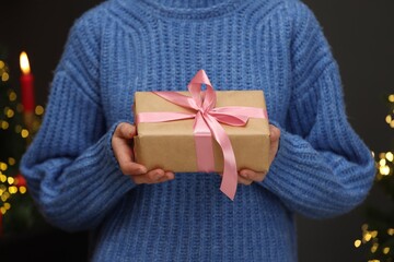 Woman with gift box in room decorated for Christmas, closeup. Bokeh effect