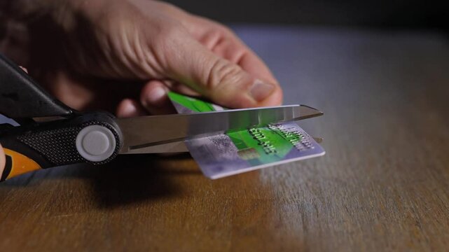 A man cuts up a credit card with a pair of scissors