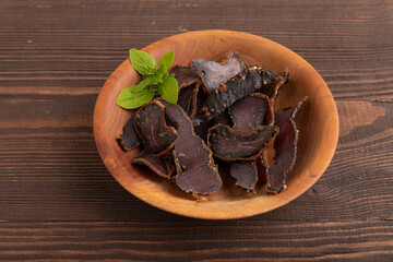Armenian Basturma dried meat on wooden bowl with pepper and herbs on brown wooden. Side view, copy space.