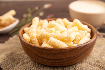 Corn flakes sticks with caramel in wooden bowl on brown wooden, Side view, close up, selective focus.