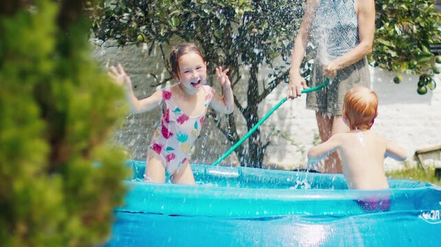 Family of mother and two kids have fun in the private pool in the green garden during summer hot day