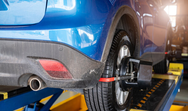 Wheel alignment equipment grip the tire of car wheel in car repair shop. Auto wheel alignment in workshop of service station. Car wheel balance. Suspension adjustment. Vehicle inside garage workshop.