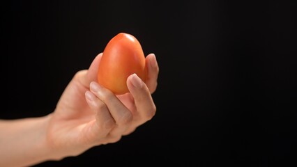Hand holding a fresh tomato on a black background culinary focus food dark environment close-up view healthy eating concept